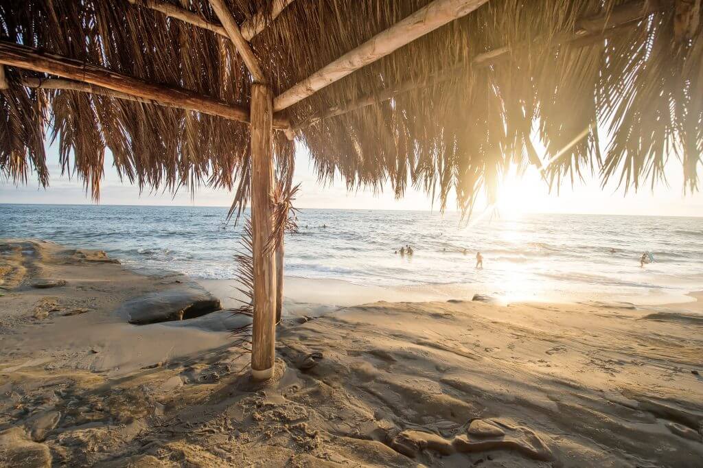 sunset on the beach from under a palm thatched cabana