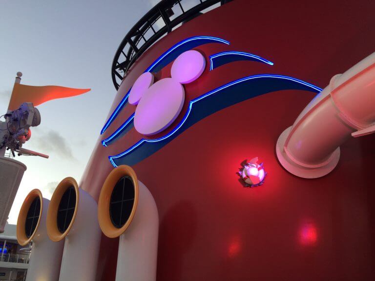 Disney Cruise Line logo on the Disney Fantasy steam stack at dawn.