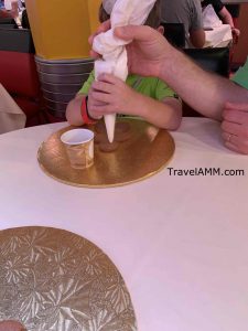 Father helping son sqeeze out the icing to decorate his gingerbread cookie on the Disney cruise line's very merrytime cruise