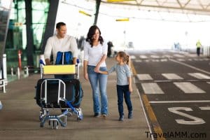 Family walking outside airport terminal with luggage