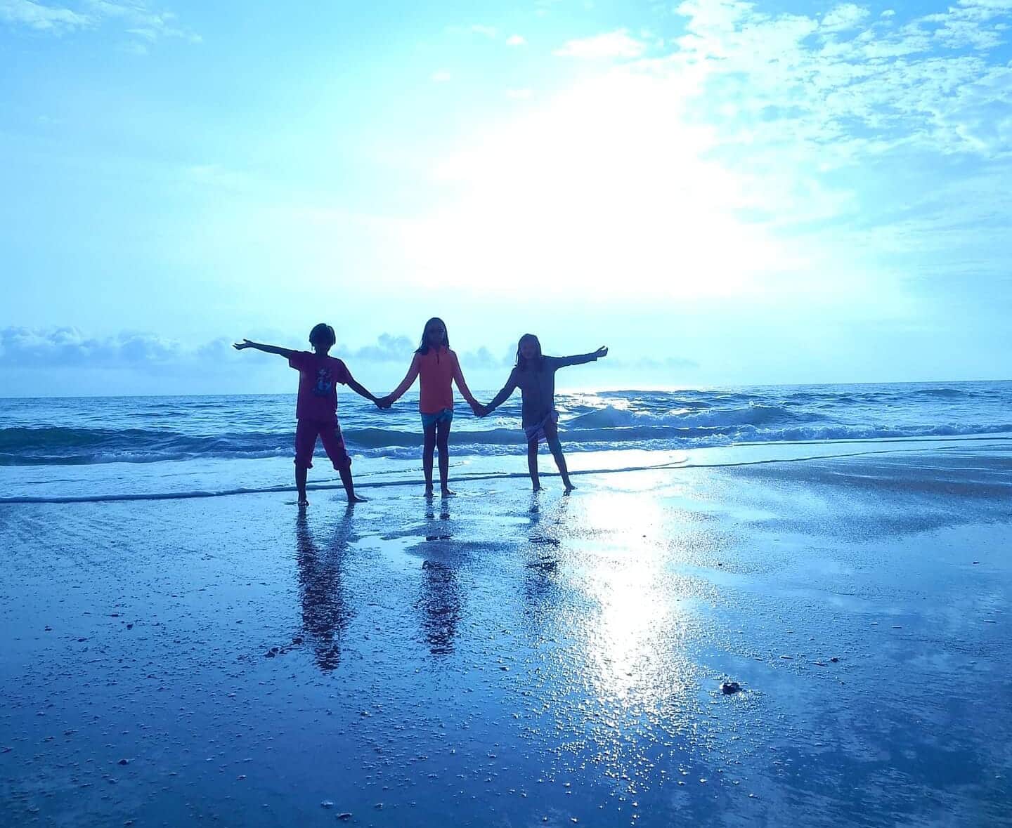 three children holding hands in silhouette on the beach